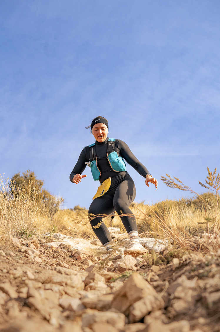 Runner in a headband descending a rocky pitch under blue sky