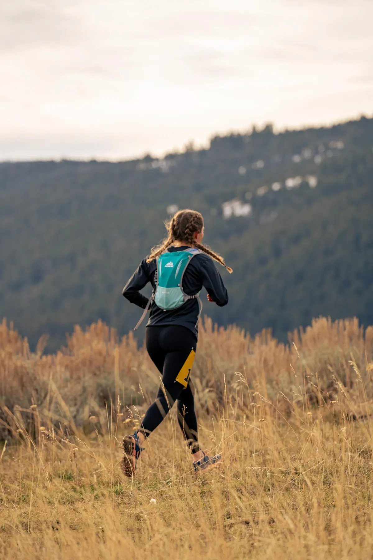 Runner with braids moving away through sage and grass