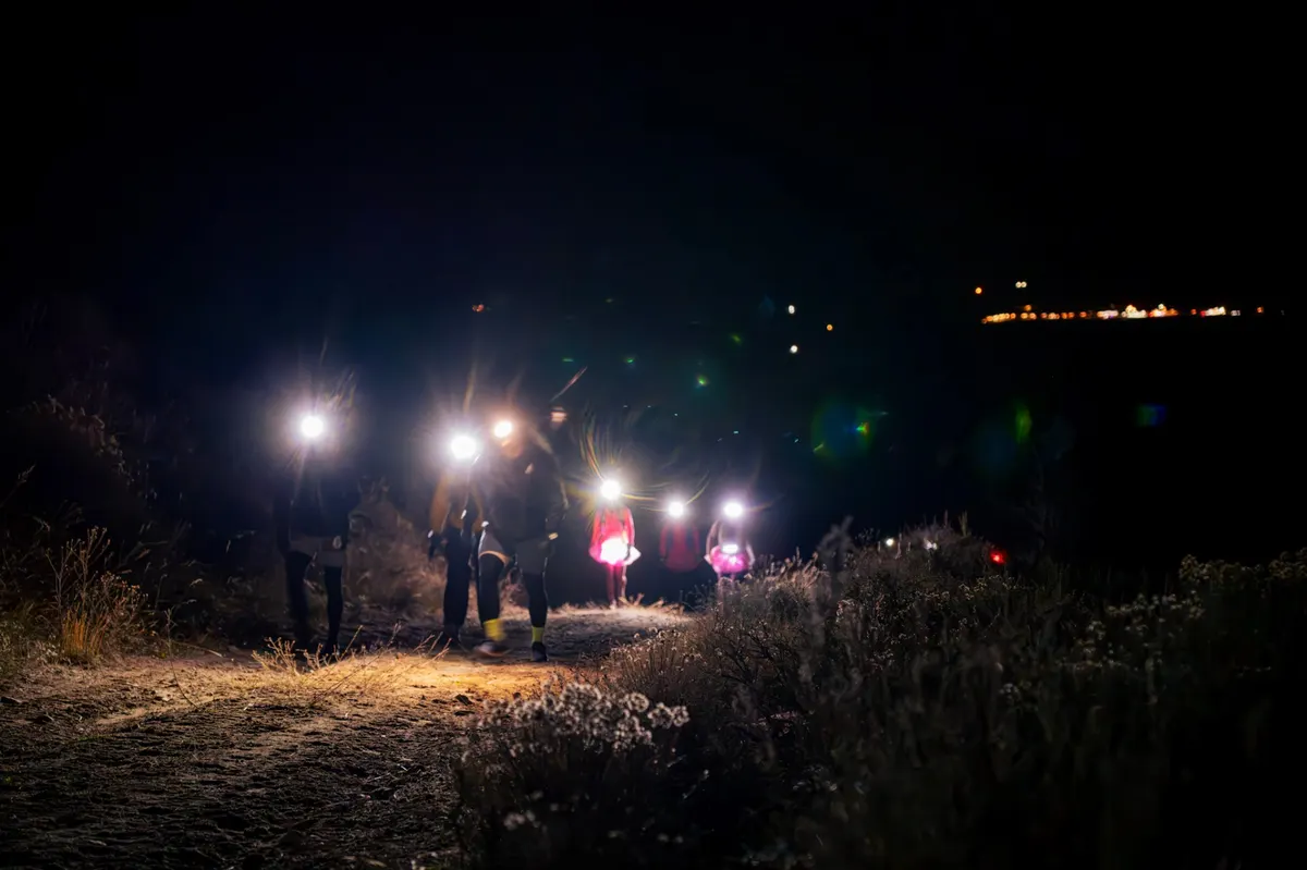 Group of runners moving up the trail with headlamps before dawn