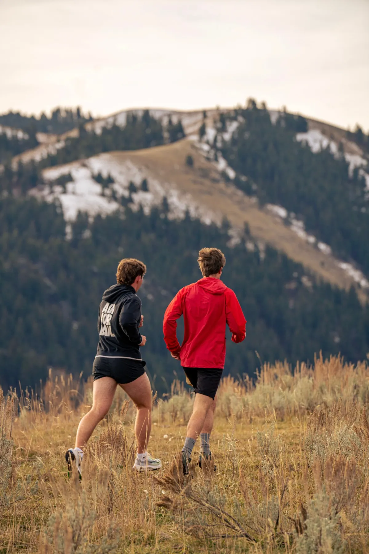 Two runners moving toward a snow-dusted ridge