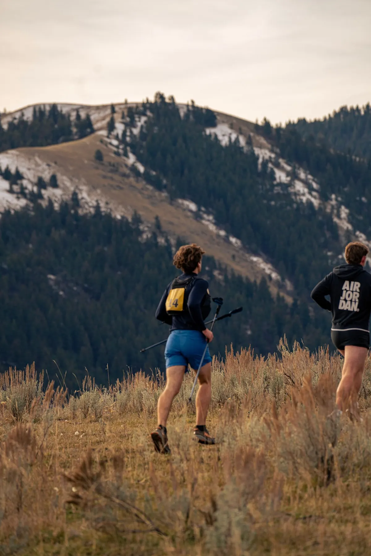 Two runners moving through sage toward snow-dusted mountains