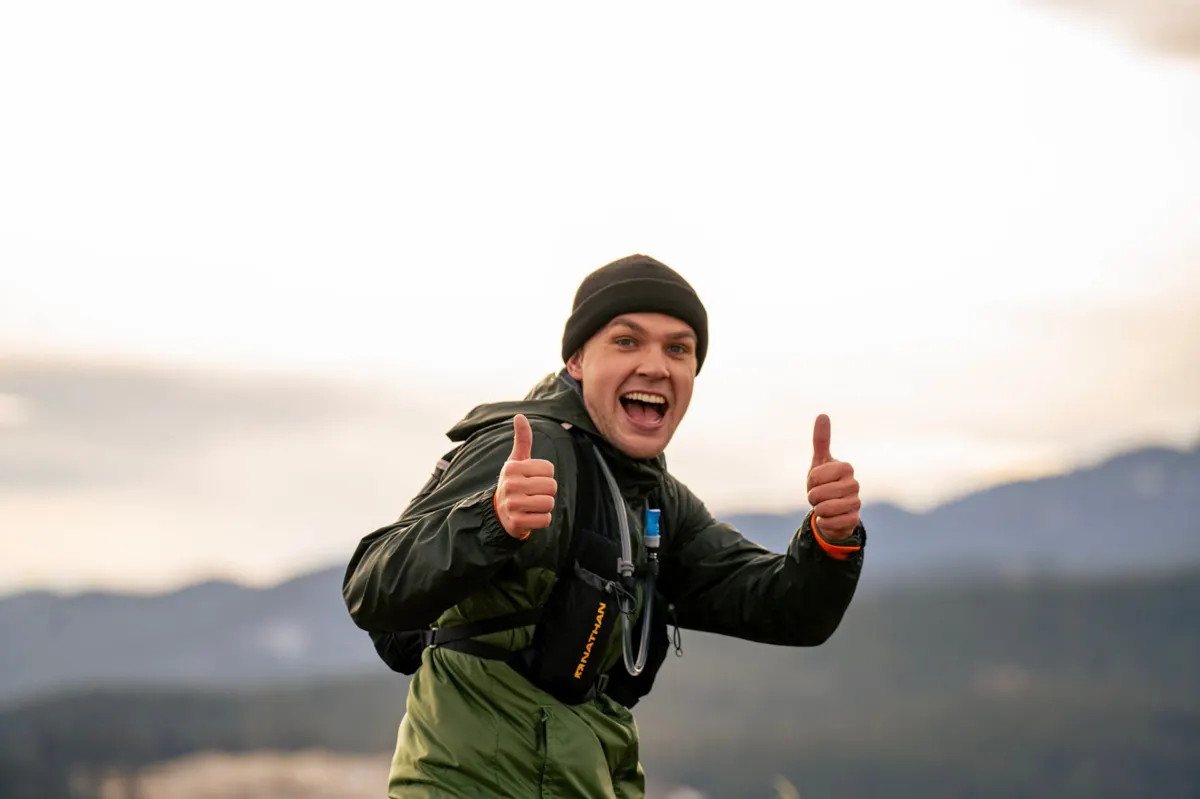 Runner grinning with two thumbs up at the summit